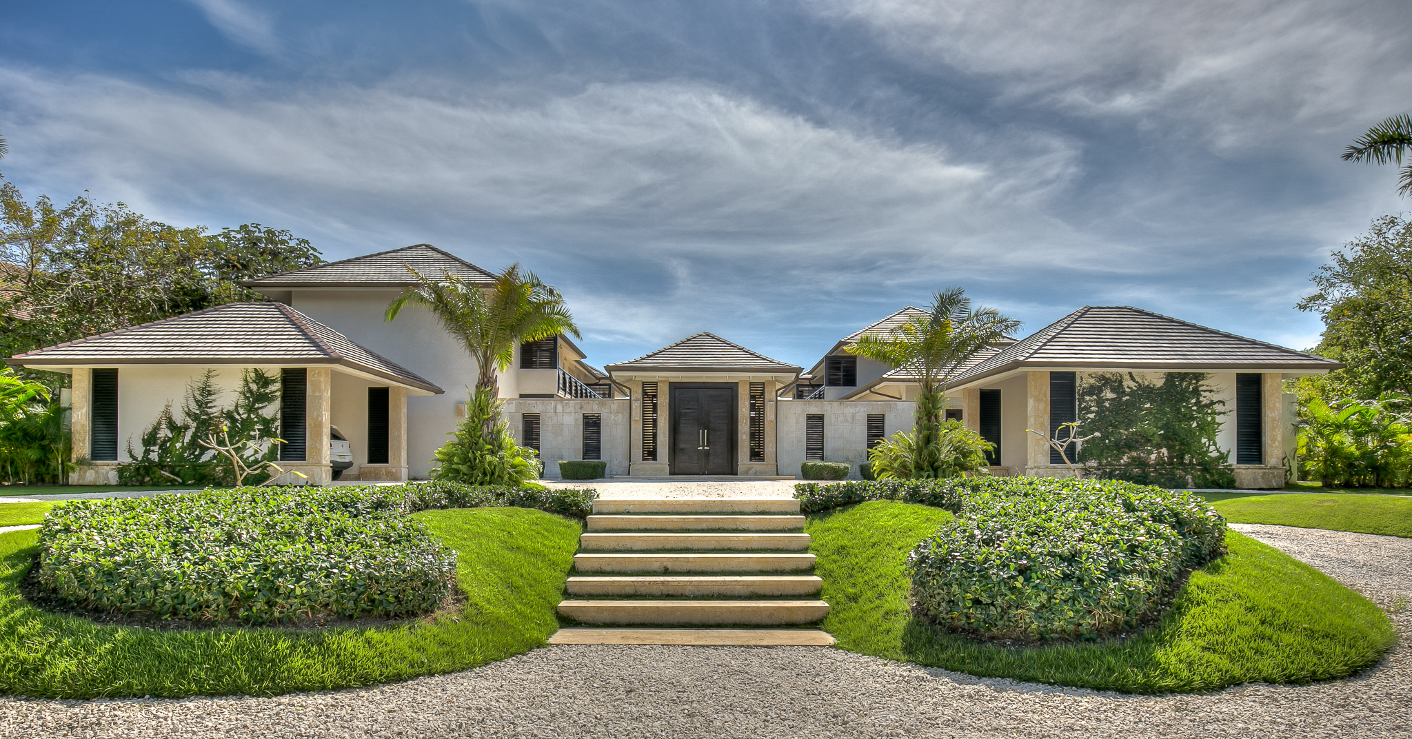 Symmetrical entrance to Casa de las Meninas with low tiled roofs, pale stone walls, shutters and landscaped steps
