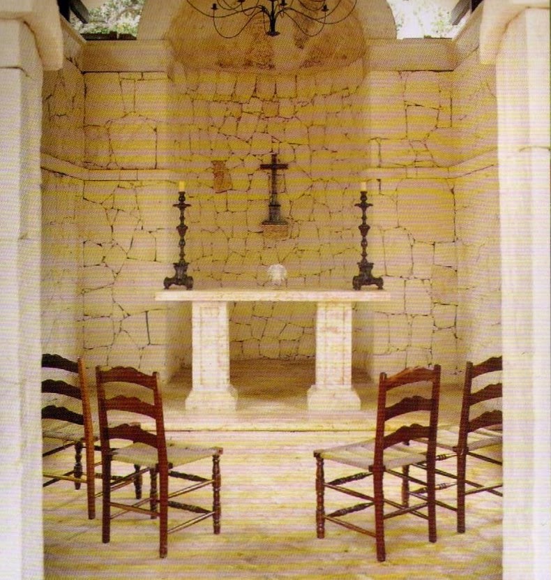 Coral-stone chapel interior with columns, a pale altar, cross and wooden chairs