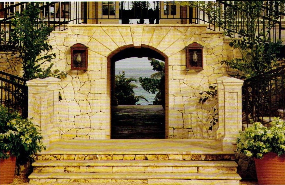 Coral-stone courtyard arch beneath a balcony framing palms and the ocean