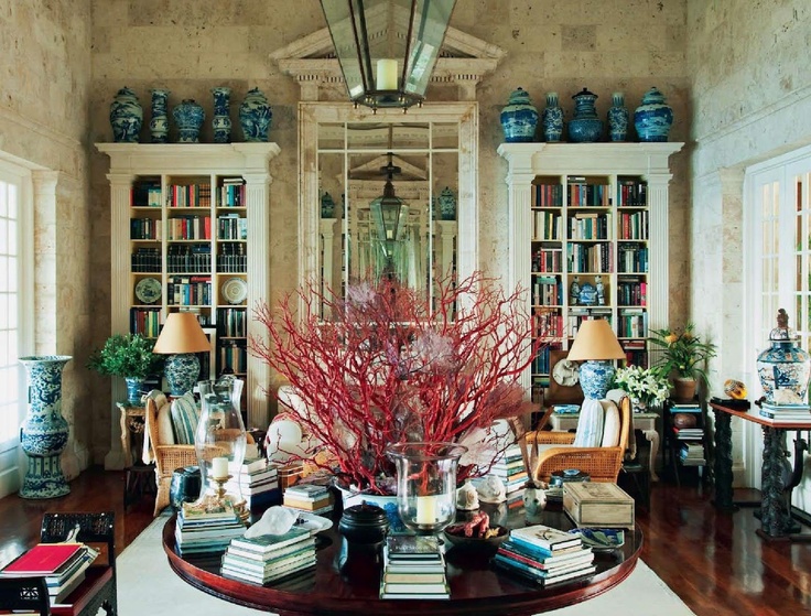 Drawing room with a central round table, books, coral-colored branches, blue-and-white porcelain and tall mirror