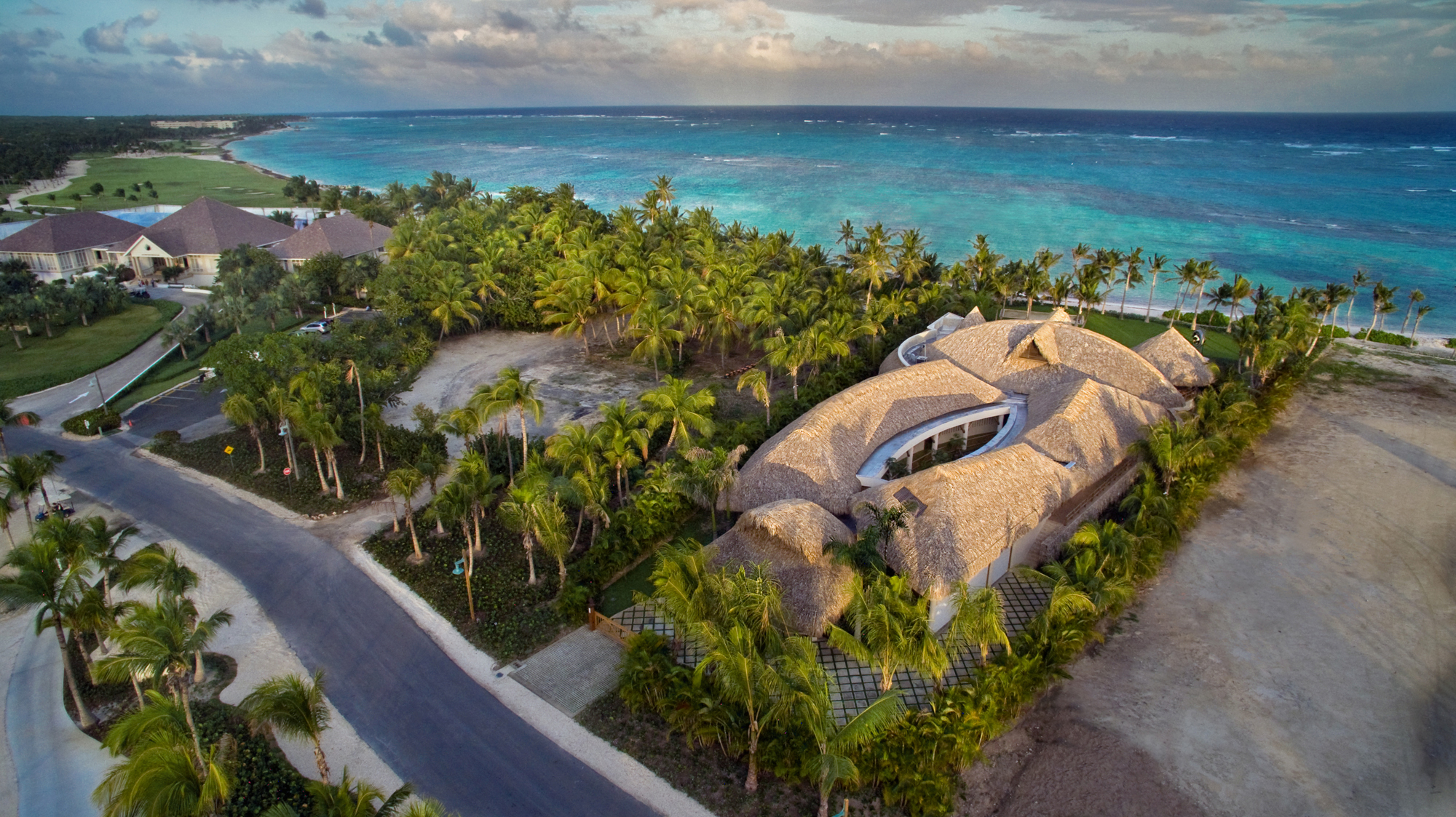 Aerial view of Sirena Blue's curved thatched roof, central courtyard, palm gardens and coastline