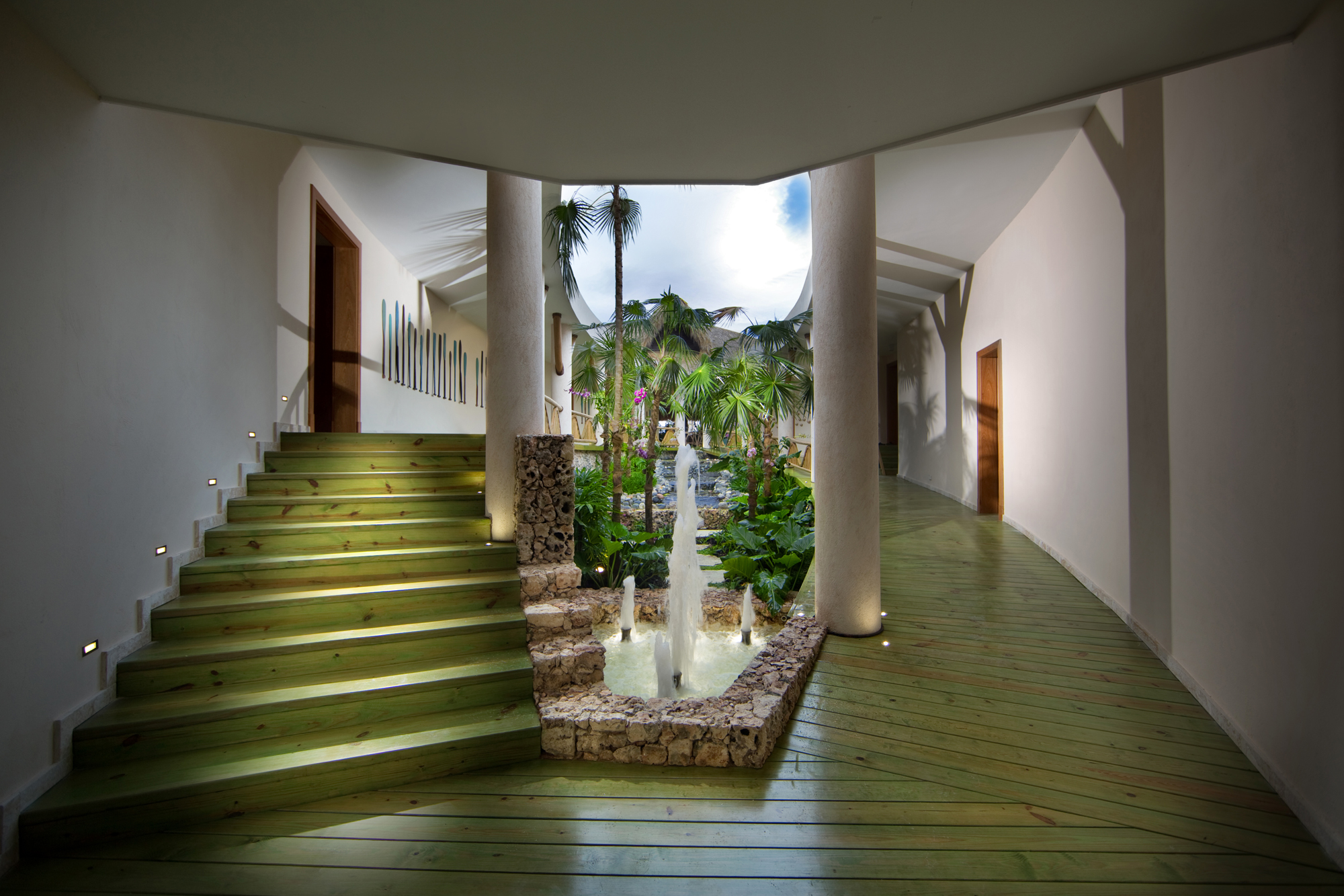 Sheltered courtyard at Sirena Blue with a stone-lined fountain, timber steps, columns and palms